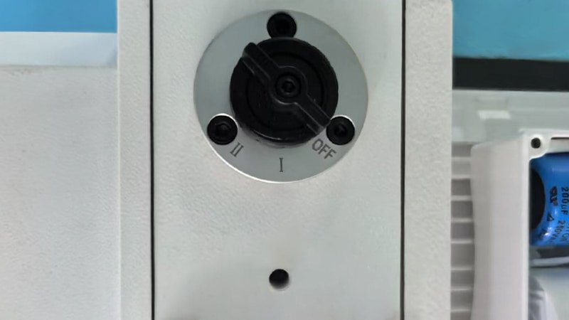 A close-up shot of a technician's hand turning a gas ballast valve on the side of a vacuum pump to the fully 