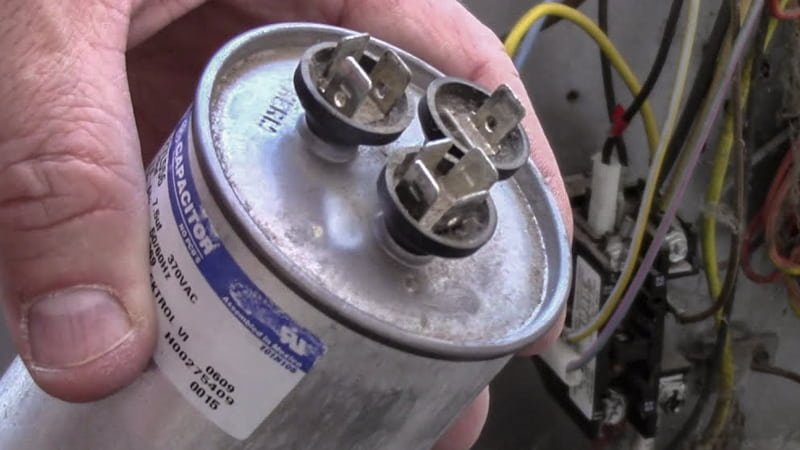 A clear photograph of a failed motor capacitor, showing its top visibly bulged or leaking a waxy substance