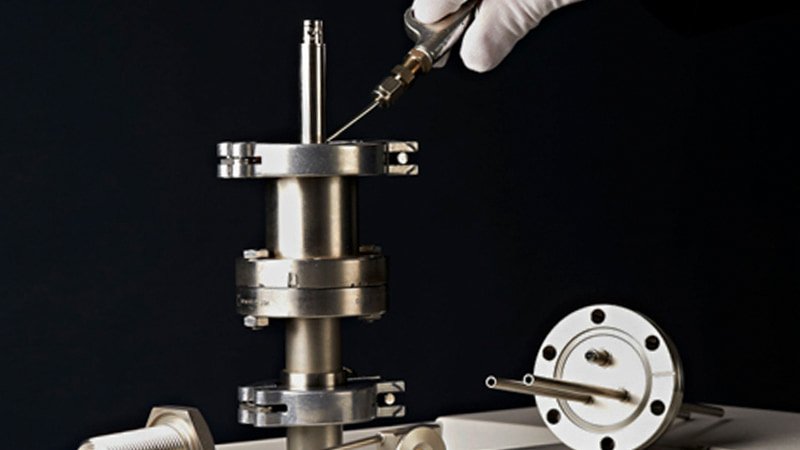 A wide shot of a modern, clean industrial laboratory with a complex vacuum chamber system at its center.