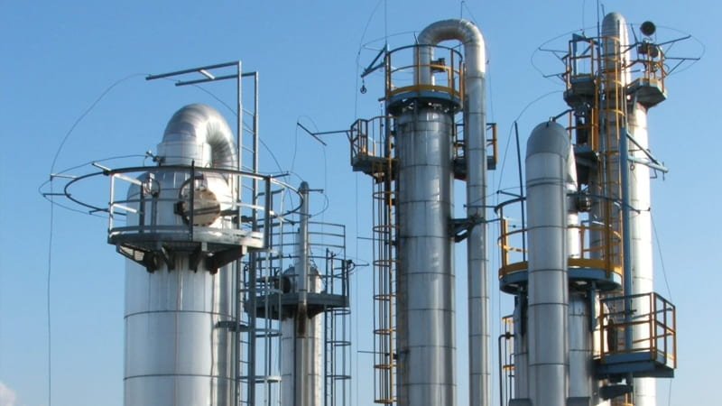 A massive, gleaming stainless-steel vacuum distillation column tower at an industrial chemical plant or oil refinery
