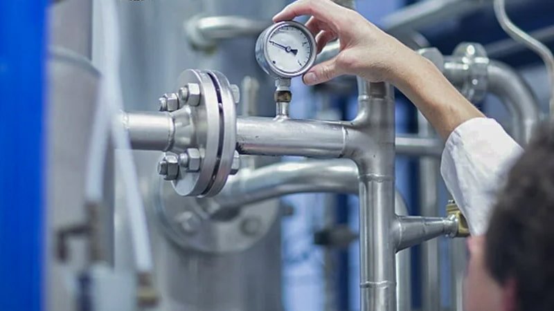A technician pointing at the digital display of a vacuum gauge showing a borderline reading like '45 microns'