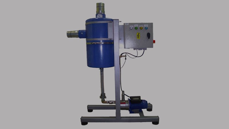 A stainless steel inline liquid separator installed on a vacuum line leading to a pump in an industrial setting. A manual drain valve is visible at the bottom