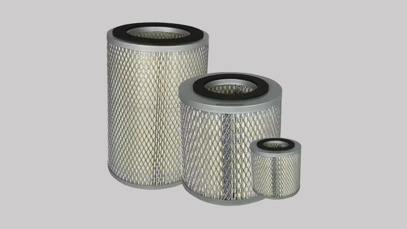A technician's hands wearing blue nitrile gloves are holding two exhaust filter elements side-by-side: one is a new, clean white filter, and the other is an old one, dark brown and saturated with oil