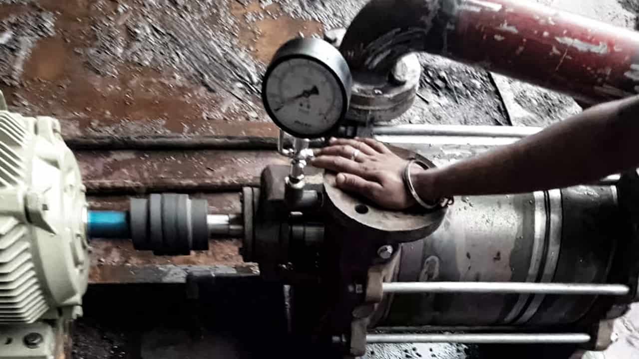 A close-up of a digital vacuum gauge screwed directly into the KF flange inlet of an industrial vacuum pump, displaying a low reading like '5 microns'