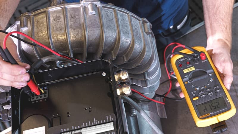 A technician in a clean industrial workshop preparing to test a recently repaired rotary vane vacuum pump, with a digital vacuum gauge and fresh oil ready