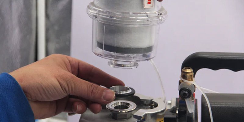 A technician's hands, wearing gloves, carefully placing a new, clean white filter element into its housing on a vacuum pump.