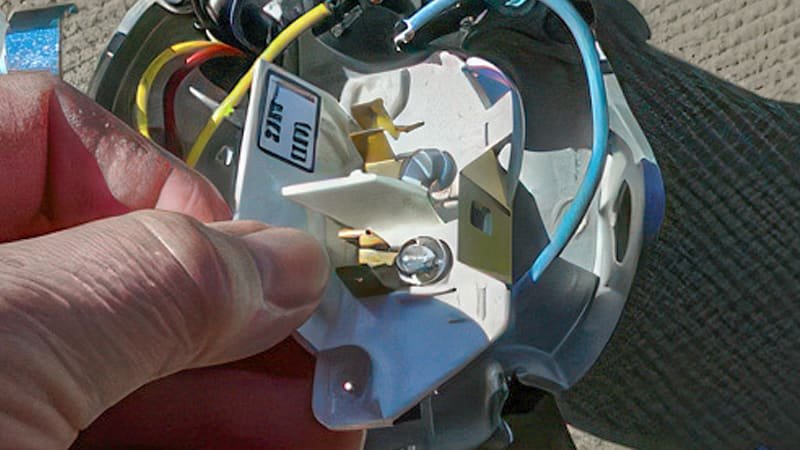 A close-up, focused shot of a technician's finger pressing the small, red thermal overload reset button on the pump's motor housing