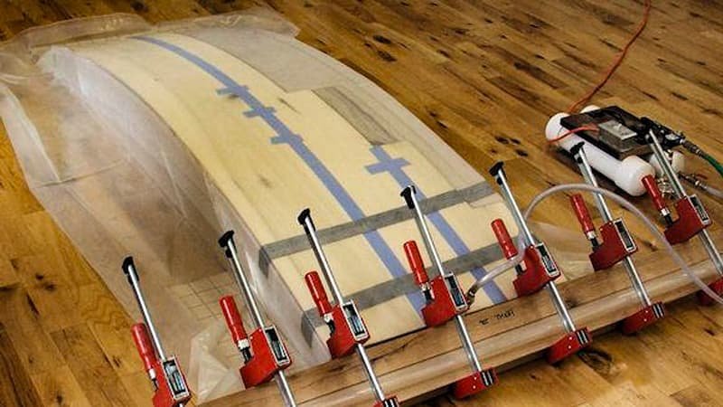 A clear diagram showing arrows representing atmospheric pressure pushing down uniformly on the outside of a vacuum bag that contains a curved woodworking mold