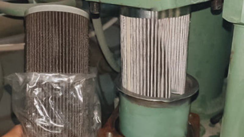 A technician holding a new, pristine vacuum filter element next to a heavily discolored and saturated used filter element, ready for disposal, emphasizing the need for replacement.