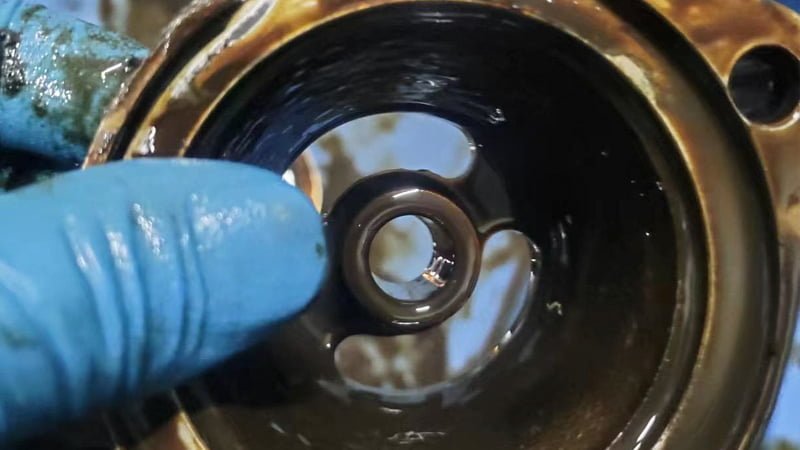A tight, focused shot on the area where the drive shaft exits the body of a vacuum pump. A single, distinct drip of dark oil is forming on the underside, indicating a failed shaft seal